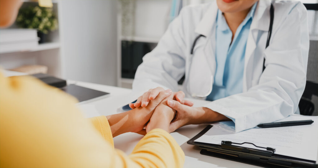 Close up of Asia female doctor in white medical uniform talk discuss touching girl patient shoulder at meeting sitting at desk in health clinic or hospital office. Psychological help concept.