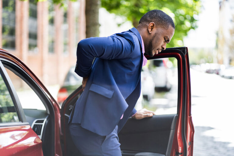 An African American man holds his back in pain after being hit from behind in a car accident.