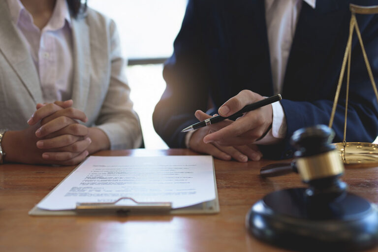 A client and her lawyer sit at a table reviewing documents.