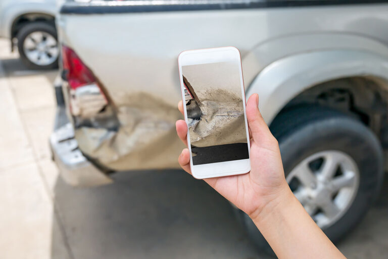 A person takes a picture of their damaged car using their smartphone.