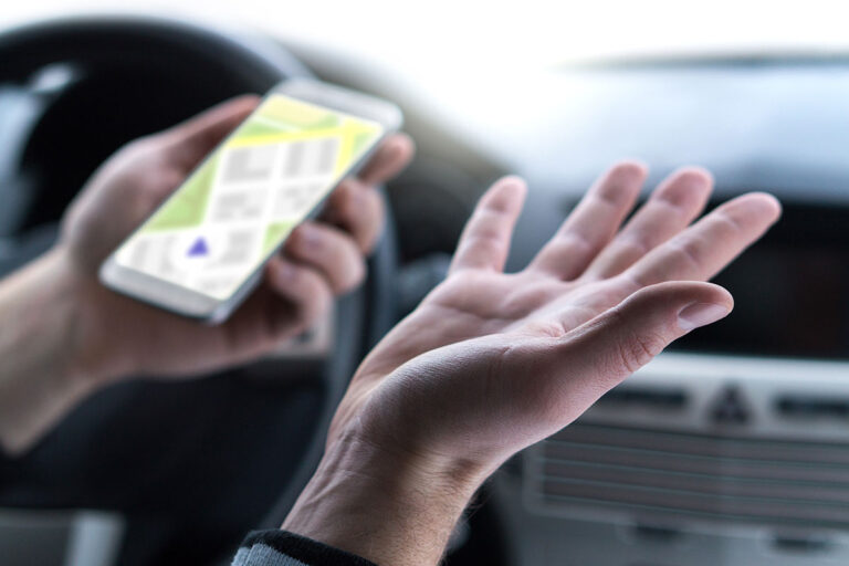 A driver holds a phone in their hands while sitting behind the wheel of their care.