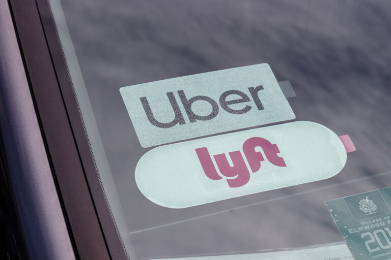 A set of Uber and Lyft stickers are displayed through a car windshield.