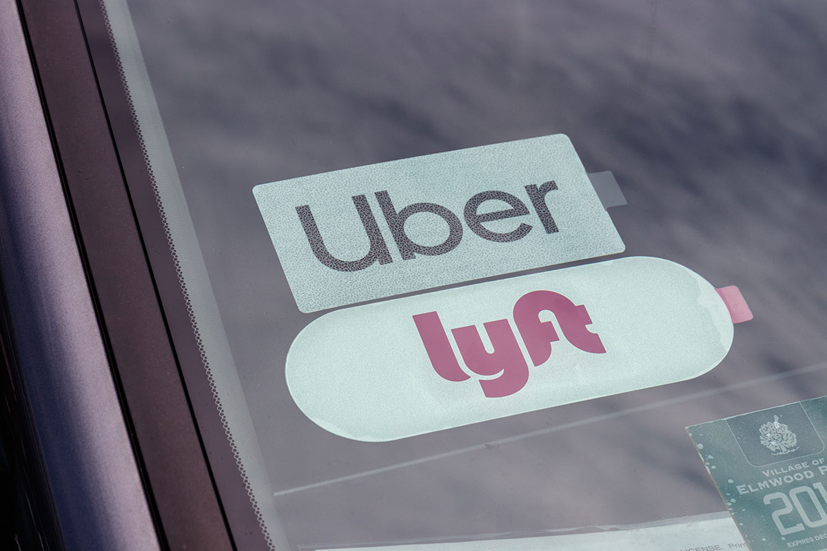 A set of Uber and Lyft stickers are displayed through a car windshield.