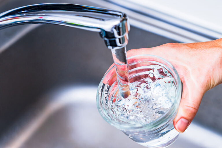 A person holds a glass of water from a faucet, highlighting concerns about PFAS contamination in drinking water.