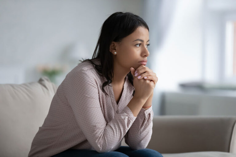 A woman sitting on a couch with a sad expression, conveying feelings of loneliness or distress.