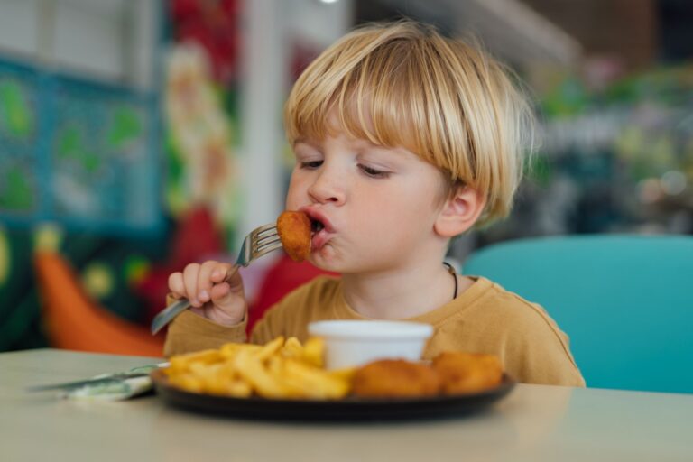 A young boy seated at a table, eating with a fork and looking content.