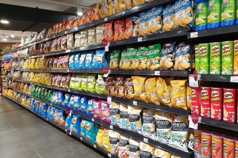 A store aisle displaying an assortment of chips and snacks, with colorful packaging visible on the shelves.
