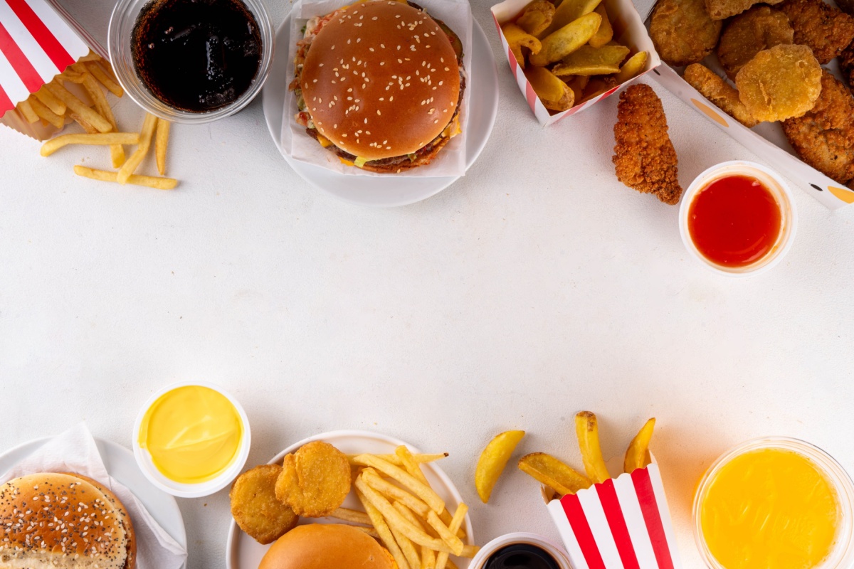 On a white table, a fast food spread includes a hamburger, fries, chicken, and ketchup and mustard for dipping.