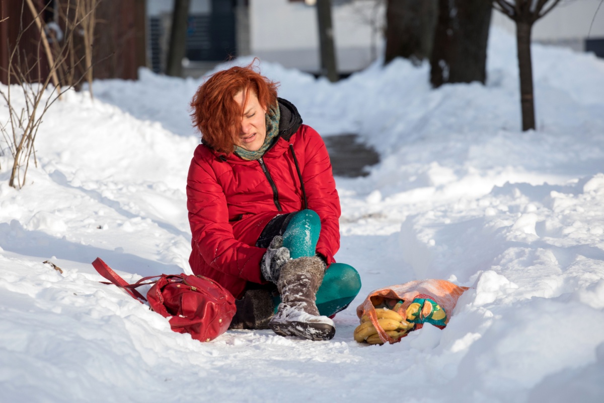 A woman sitting in the snow with an injured ankle, holding a bag, surrounded by a winter landscape.