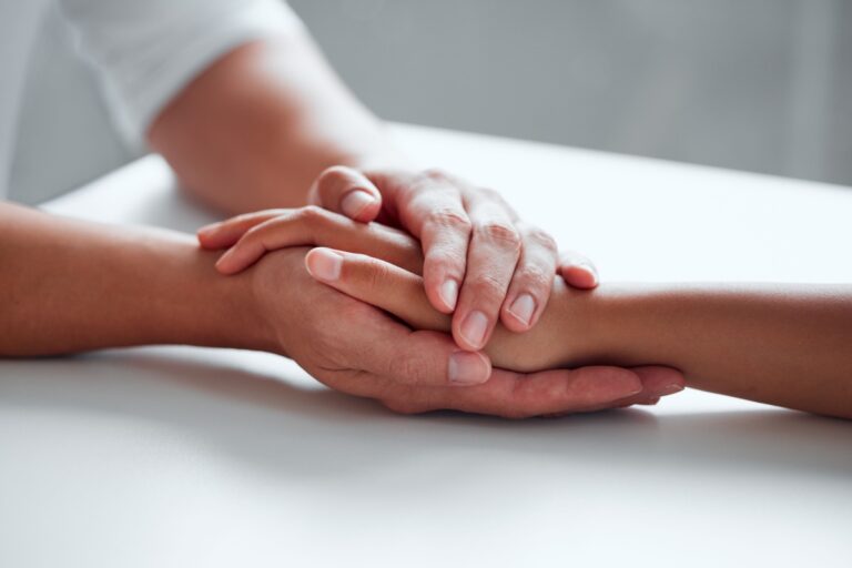 A person gently holds the hand of another, symbolizing support and connection between them.