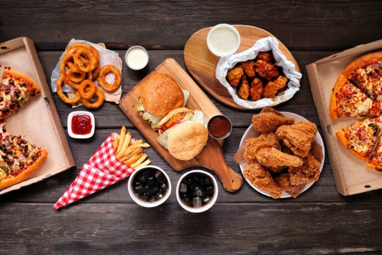 A spread of fast food items featuring pizza, chicken wings, fries, and onion rings on a table.