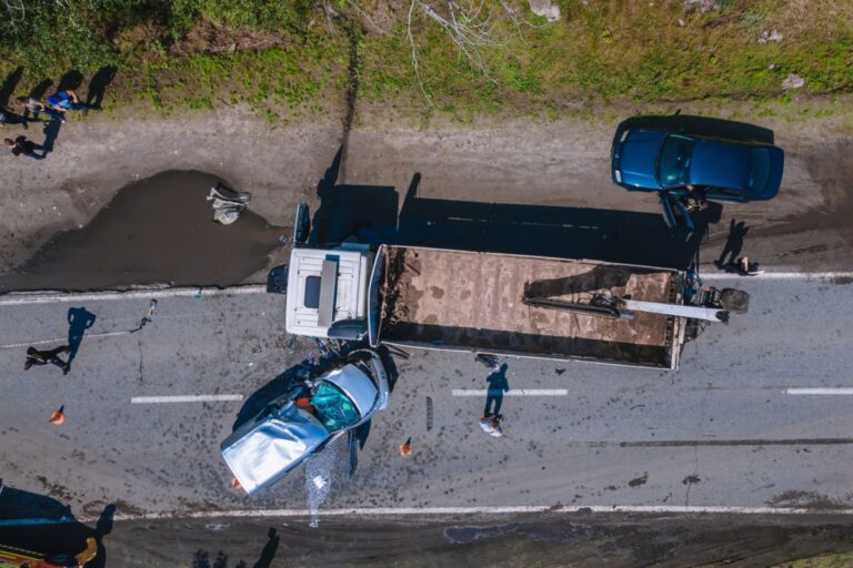 Aerial view of a truck and a car accident on a road surrounded by greenery.