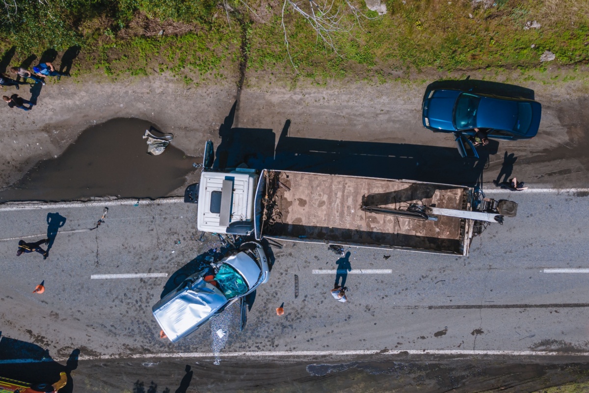 Aerial view of a truck and a car accident on a road surrounded by greenery.