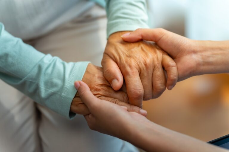 A woman gently holds the hand of an elderly person, symbolizing care and support in their relationship.