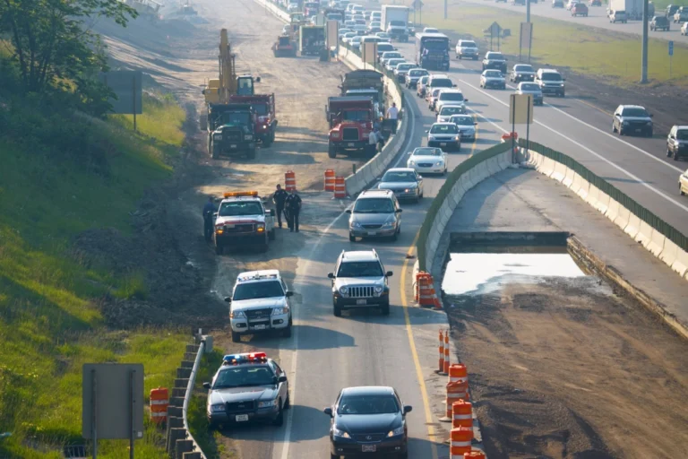 A construction zone on a highway featuring machinery and vehicles, illustrating the complexities of driving in such areas.