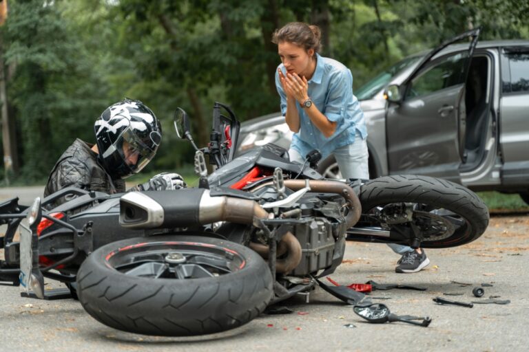 A woman expresses concern to a man sitting beside a motorcycle, who appears injured after their accident.