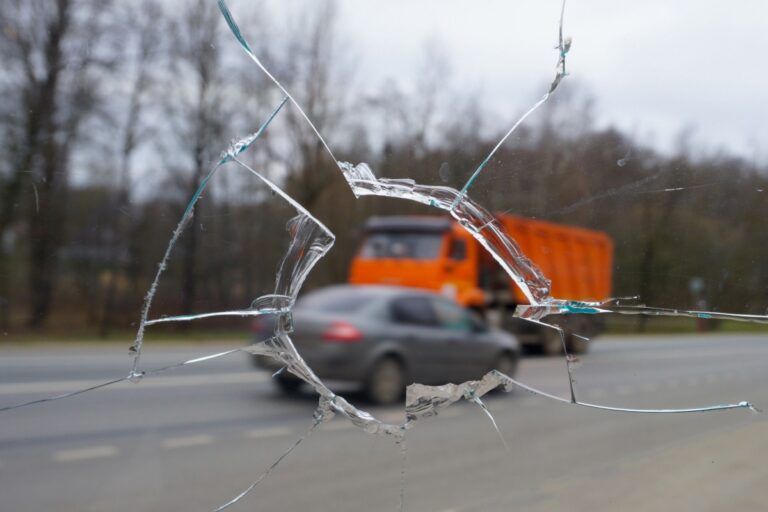 A broken windshield with a truck driving past, highlighting the aftermath of a truck accident involving unsecured cargo in Ohio.