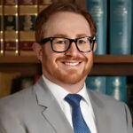 Attorney Brandon Dean, in a suit and glasses, smiles confidently for the camera.
