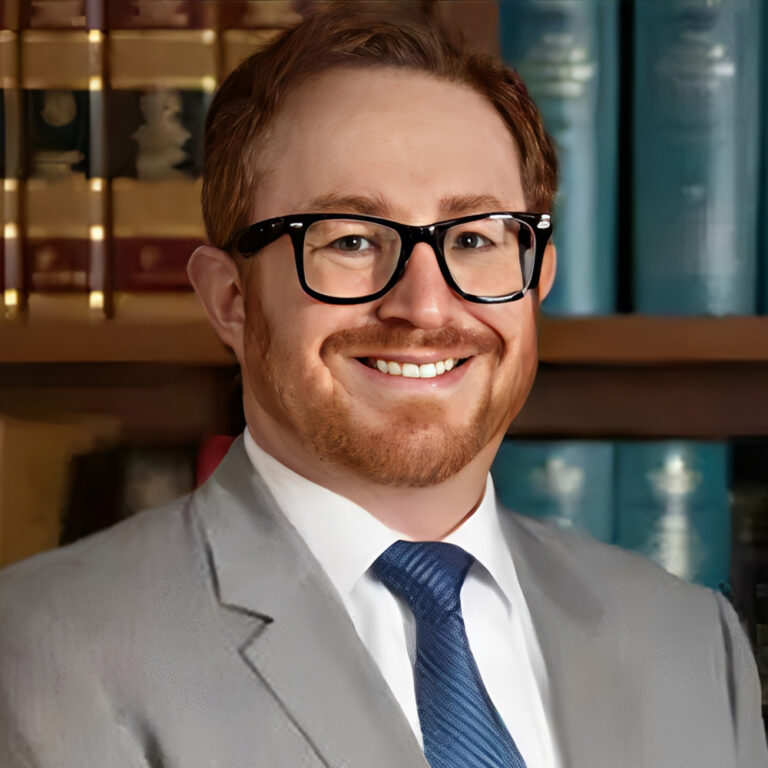 Attorney Brandon Dean, in a suit and glasses, smiles confidently for the camera.