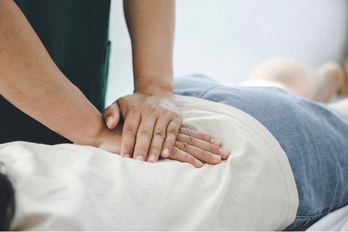 A chiropractor examines a patients back and applies therapy with her hands.