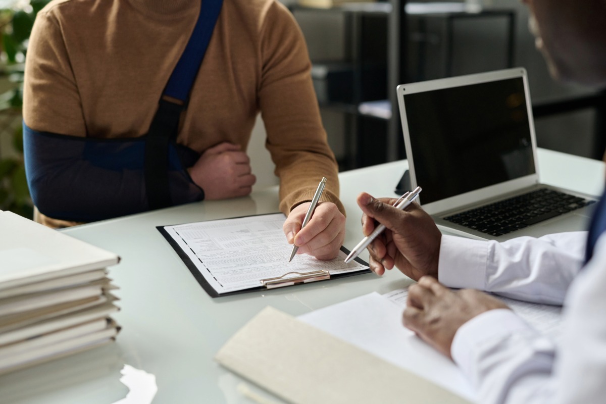 An injured woman with her arm in a sling sits at a table discussing her case with her lawyer.