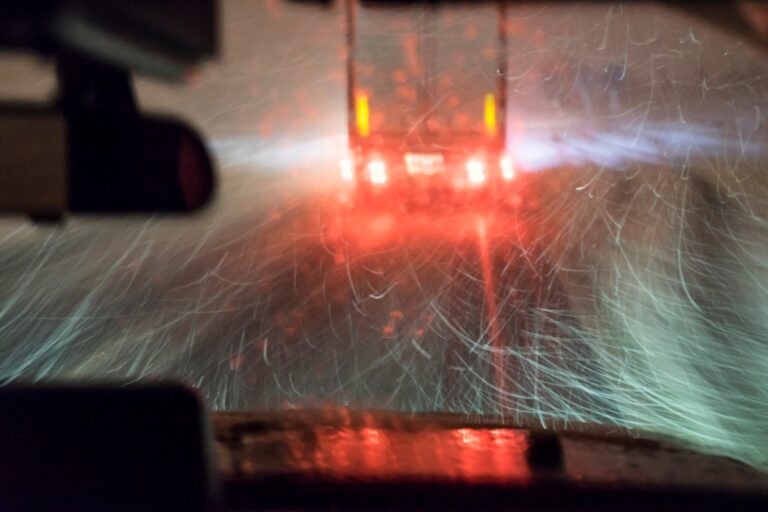 Driver following a tractor trailer on a snowy highway at night.