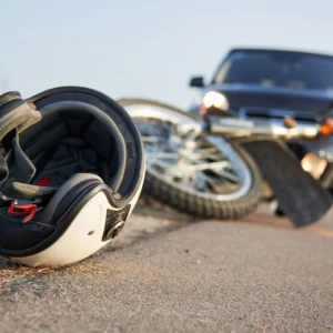 A motorcycle helmet is positioned on the ground next to a car, indicating a potential motorcycle accident scene.