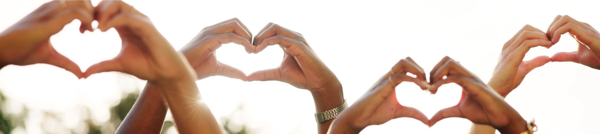 Multiple hands make heart shapes with the sun behind them