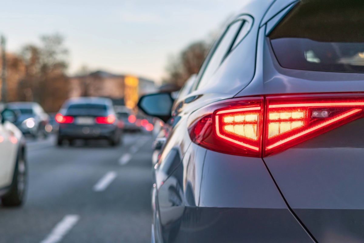 A close-up image of a silver car's brake lights while driving on an urban street in traffic.