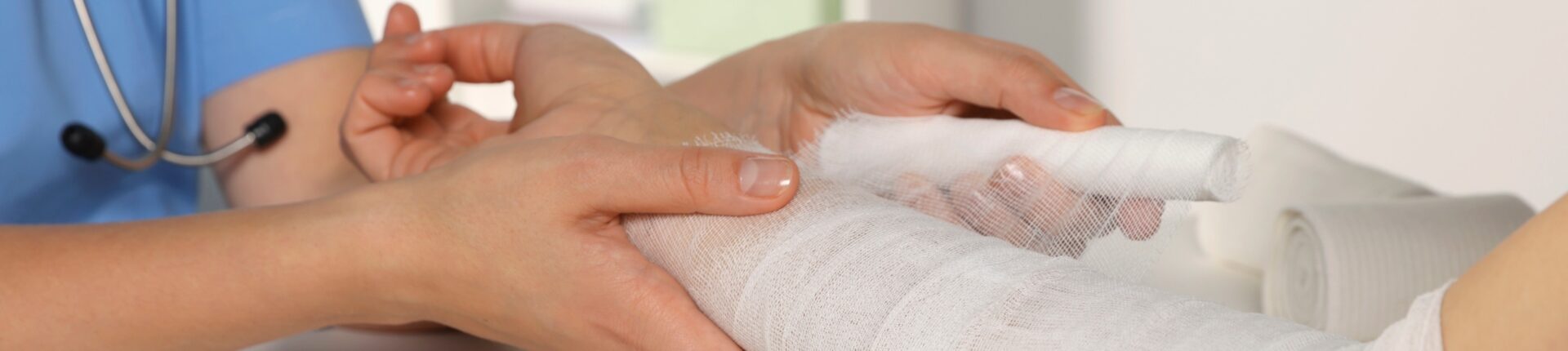 A healthcare professional in blue scrubs is gently wrapping an arm in a white bandage, conveying care and protection in a medical setting.