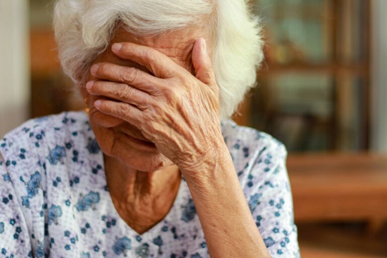 An elderly woman with her hands over her face, symbolizing emotional pain and the impact of elder abuse.