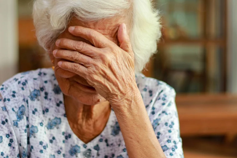 An elderly woman with her hands over her face, symbolizing emotional pain and the impact of elder abuse.