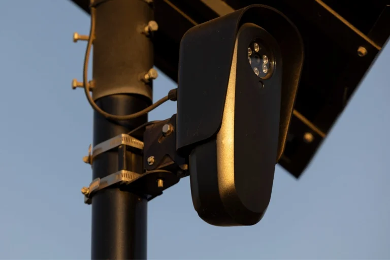Pole-mounted security camera with solar panel overlooking a city street at sunset, used for automated license plate reading related to Flock cameras Ohio.